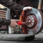 A mechanic wearing gloves is using a tool to work on a car's brake disc in a garage.