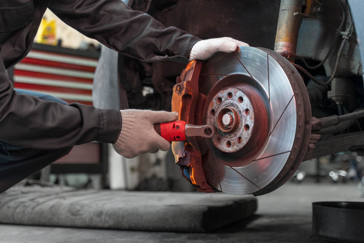 A mechanic wearing gloves is using a tool to work on a car's brake disc in a garage.
