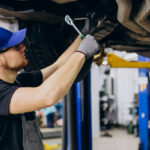 Mechanic wearing a blue cap and gloves works under a vehicle to fix Bad or Dirty Fuel Injectors.