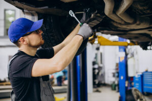 Mechanic wearing a blue cap and gloves works under a vehicle to fix Bad or Dirty Fuel Injectors.