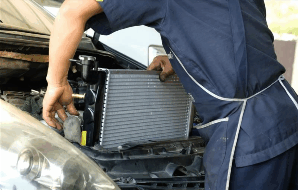 A car mechanic installs a new radiator in a car's engine bay in a Las Vegas shop, focused on aligning it properly for maintenance.