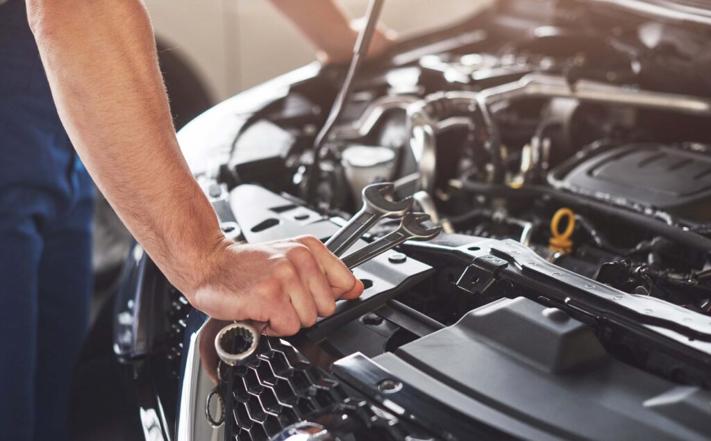 A mechanic is worked on the open engine compartment of a car, holding a wrench and Disassemble components of a car engine in the Las Vegas workshop.