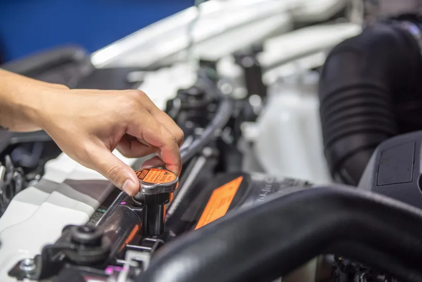 A mechanic's hand is removing the radiator cap from an open car engine for maintenance in a Las Vegas garage.