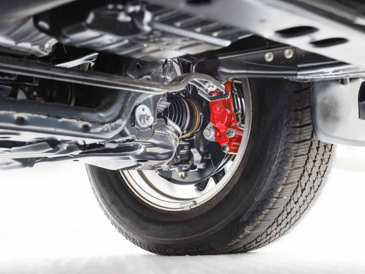 Close-up of a car's underside, showcasing the wheel, tire, and red brake caliper against a metallic frame.