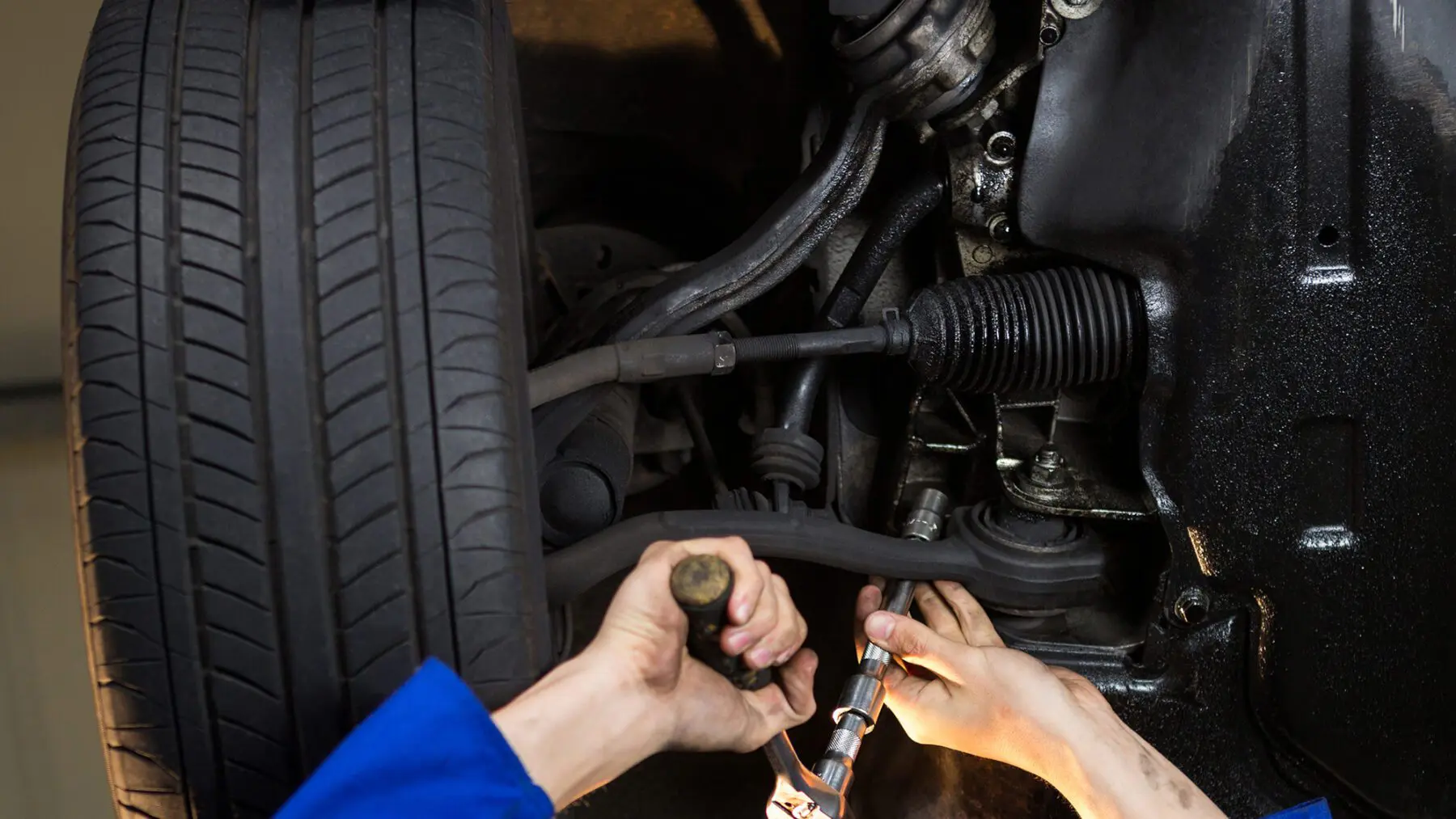 A mechanic in Las Vegas garage is working under a car, using tools to repair the suspension components near the tire.
