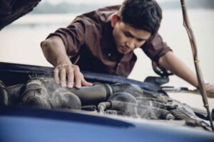 A person inspects a car engine, with steam rising from it, indicating a potential issue or overheating.